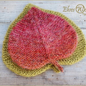 K&ouml;nnte beinhalten: Ein gestricktes Blatt mit einer roten und orangenen Mitte und einem gr&uuml;nen Au&szlig;enrand. Das Blatt liegt auf einer Holzoberfl&auml;che. Der Text "Elves World Toys & Patterns" befindet sich in der oberen rechten Ecke des Bildes.