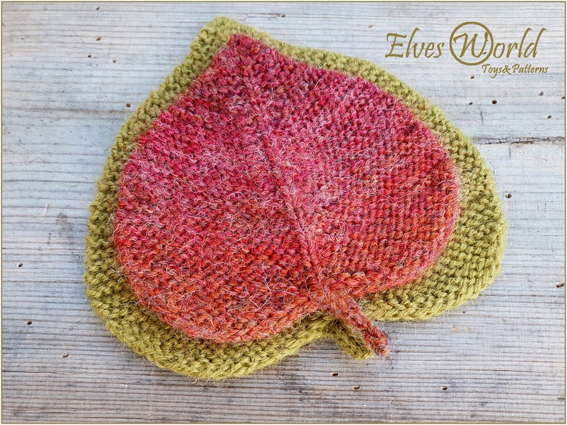 K&ouml;nnte beinhalten: Ein gestricktes Blatt mit einer roten und orangenen Mitte und einem gr&uuml;nen Au&szlig;enrand. Das Blatt liegt auf einer Holzoberfl&auml;che. Der Text "Elves World Toys & Patterns" befindet sich in der oberen rechten Ecke des Bildes.