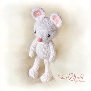 K&ouml;nnte beinhalten: Ein wei&szlig;es, gestricktes Mausschmusetier mit rosa Ohren und einer rosa Nase. Das Spielzeug steht auf einer wei&szlig;en, flauschigen Oberfl&auml;che. Der Text "Elves World Toys & Patterns" ist in der rechten unteren Ecke des Bildes zu sehen.