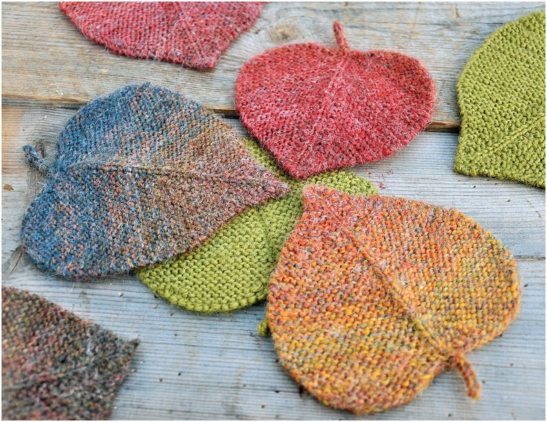 K&ouml;nnte beinhalten: Sechs gestrickte Untersetzer in Blattform in verschiedenen Farben, darunter Gr&uuml;n, Blau, Orange und Rot.