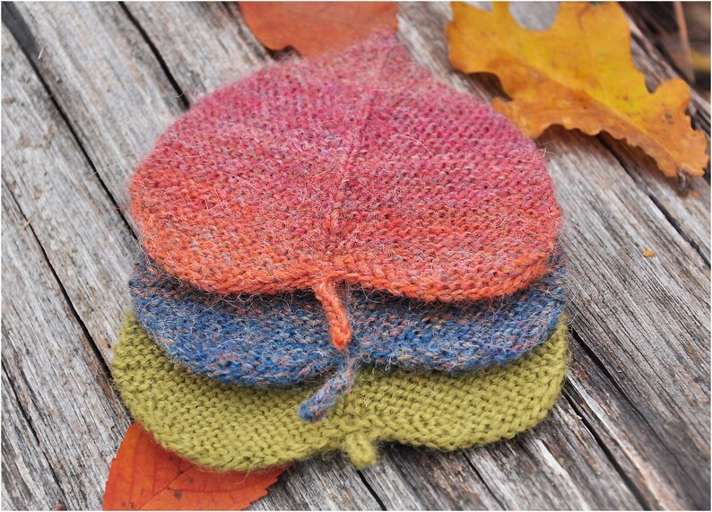 K&ouml;nnte beinhalten: Drei gestrickte Untersetzer in Blattform in den Farben Gr&uuml;n, Blau und Orange. Die Untersetzer sind &uuml;bereinander gestapelt.