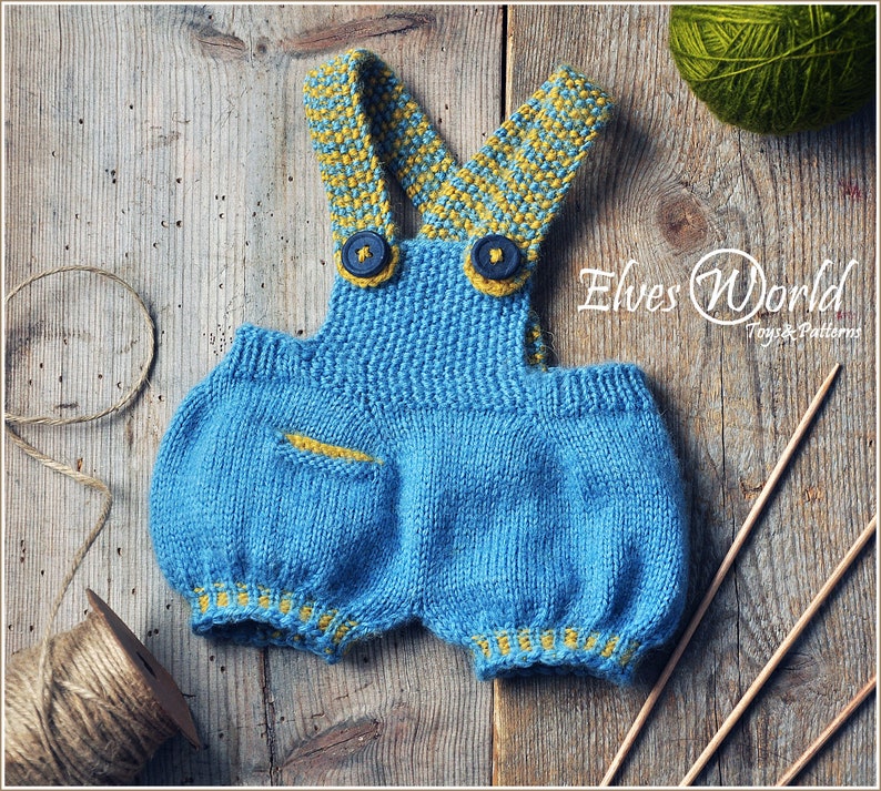 May include: Knitted blue baby dungarees with yellow and blue striped straps and yellow trim. The dungarees have a small pocket on the front. The image also includes yarn and knitting needles.