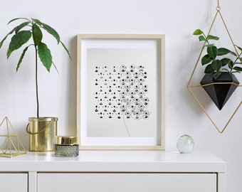 May include: A framed black and white abstract art print featuring a cluster of small, stylized figures. The artwork is displayed on a white surface with a gold geometric sculpture, a small glass jar, and a potted plant in a gold container. A hanging planter with a black geometric pot and a small plant is also visible.