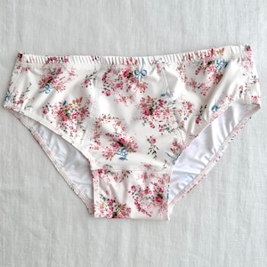 Puede incluir: Bragas blancas con estampado floral en rosa, azul y verde. La ropa interior tiene un corte clásico con cintura y aberturas de piernas cómodas. El diseño floral se extiende por toda la superficie de la ropa interior.