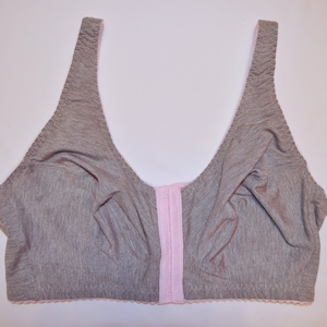 May include: A gray bra with a pink front closure and trim. The bra has wide straps and a soft, comfortable appearance. The design is simple and functional, suitable for everyday wear.