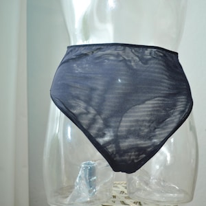 Op de afbeelding: Donker marineblauwe slip met hoge taille, weergegeven op een doorzichtige mannequin. De transparante stof heeft een subtiel gestreept patroon. De achtergrond omvat een wit gordijn en een groene plant.
