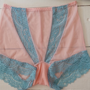 May include: A pair of pink underwear with teal lace trim. The underwear features a sheer pink fabric with teal lace accents along the edges and down the front. The lace has a floral design.