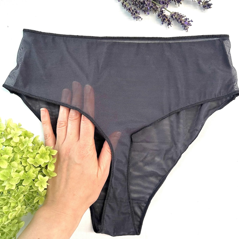 Op de afbeelding: Donkergrijze, doorschijnende high-waisted onderbroek. Het ondergoed is gemaakt van een lichtgewicht, doorzichtige stof. De afbeelding bevat ook takjes lavendel en groene bladeren.