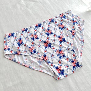 May include: White underwear with a floral pattern featuring red and blue roses. The roses are set against a trellis design with blue leaves. The underwear is made of a soft, lightweight fabric.