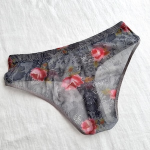 Peut inclure: Sous-vêtements gris avec un motif floral de roses roses. La lingerie délicate présente une superposition de dentelle et une coupe haute. Le tissu transparent offre une esthétique douce et féminine.