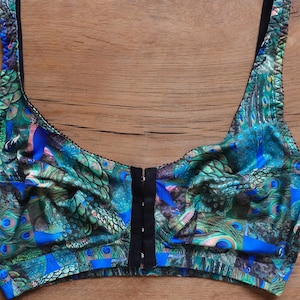 May include: A black bra with adjustable straps and a front closure. The bra is made of a soft, stretchy fabric with a peacock feather print in shades of green, blue, and black.