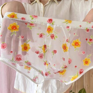 Puede incluir: Ropa interior blanca transparente con un patrón floral de narcisos amarillos y flores rosas.