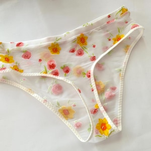 Könnte beinhalten: Weiße, durchsichtige Unterwäsche mit einem Blumendruck mit gelben und rosa Blüten.
