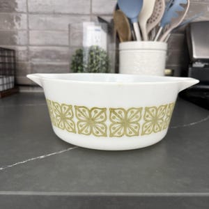 May include: White casserole dish with a floral pattern in shades of green. The dish has two handles and is likely made of ceramic or glass. The floral design is repeated around the dish's exterior.
