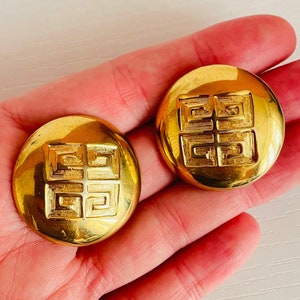 Pendientes de clip con botón en tono dorado con logo de caja 4G de Givenchy, grandes, gruesos, redondos, resistentes y con diseño de letra G prensada.