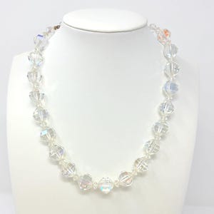 May include: A clear, faceted crystal bead necklace displayed on a white bust. The beads are strung together, reflecting light and creating a shimmering effect. The necklace is a delicate piece of jewelry.