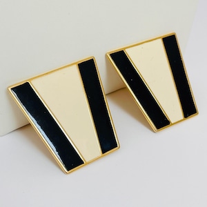 May include: A pair of gold-toned earrings with black and white geometric designs. The earrings are shaped like a triangle with rounded corners.