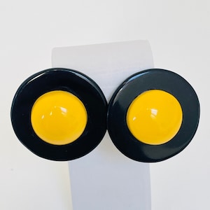 Op de afbeelding: Een paar ronde oorbel studs in zwart en geel. De oorbellen zijn gemaakt van plastic en hebben een eenvoudig ontwerp.