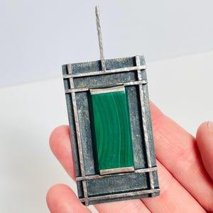 Può includere: Un ciondolo d'argento con una pietra di malachite verde incastonata in una cornice geometrica.