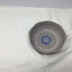 May include: A white ceramic bowl with a blue and white floral design. The bowl has a speckled glaze and a slightly irregular shape.