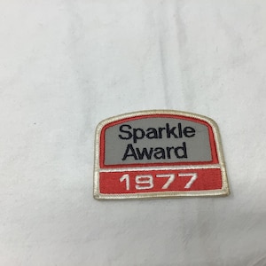 May include: A red and white embroidered patch with the text "Sparkle Award 1977".
