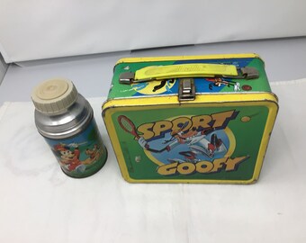 May include: Vintage metal lunchbox and thermos featuring Goofy playing sports. The lunchbox is yellow, green, and blue with the text "Sport Goofy". The thermos is silver with a white lid and features Goofy and Mickey Mouse playing golf.