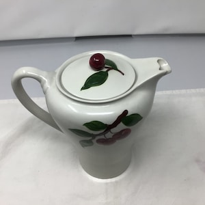 May include: White ceramic teapot with a cherry design. The teapot has a lid with a single cherry on top and a branch of cherries on the side.