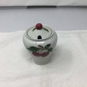 May include: White ceramic sugar bowl with a lid. The lid has a red cherry on top. The bowl has a green leaf and red cherry design.