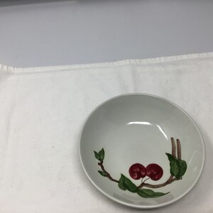May include: A white ceramic bowl with a green and red cherry design. The bowl is round and has a slight lip.