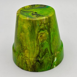 May include: A small, green and yellow marbled ceramic flower pot. The pot has a flared shape with a small base and a hole in the center of the top. The colors swirl together, creating a unique pattern.