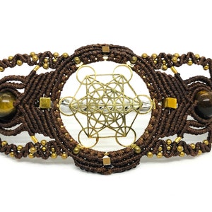 May include: Brown macrame bracelet with gold beads and a gold metal geometric design. The bracelet features two tiger's eye stones.