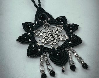 May include: Black macrame necklace with a silver Metatron's Cube pendant. The necklace features black beads and silver accents, with a starburst design around the pendant. The pendant is a geometric design.