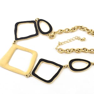 May include: Gold-tone necklace featuring geometric shapes with black enamel accents. The necklace has a chain with an adjustable length and a lobster clasp closure. The design includes open squares and ovals.