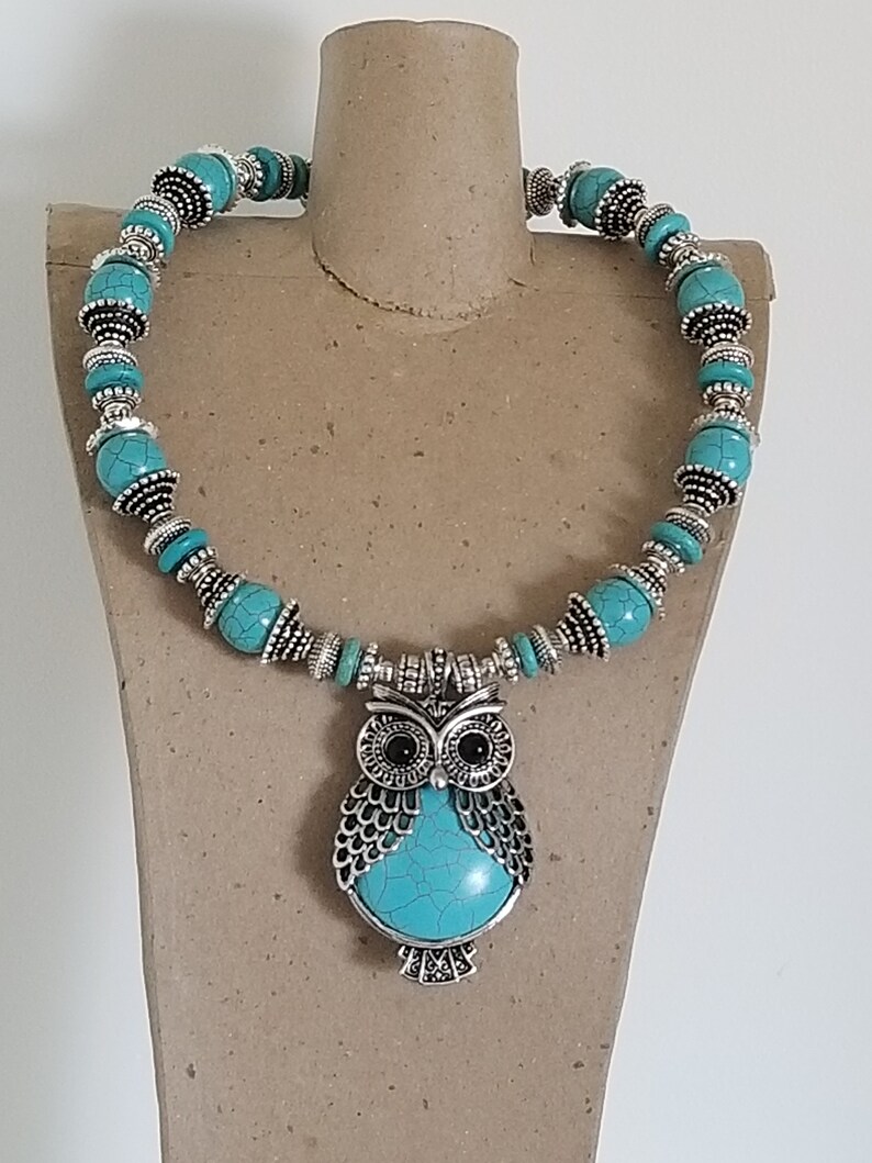 May include: A turquoise and silver necklace with an owl pendant. The owl has black eyes and a turquoise body.