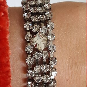 Peut inclure: Un bracelet argent&eacute; avec une rang&eacute;e de strass transparents. Le bracelet a un grand strass de forme carr&eacute;e au centre.