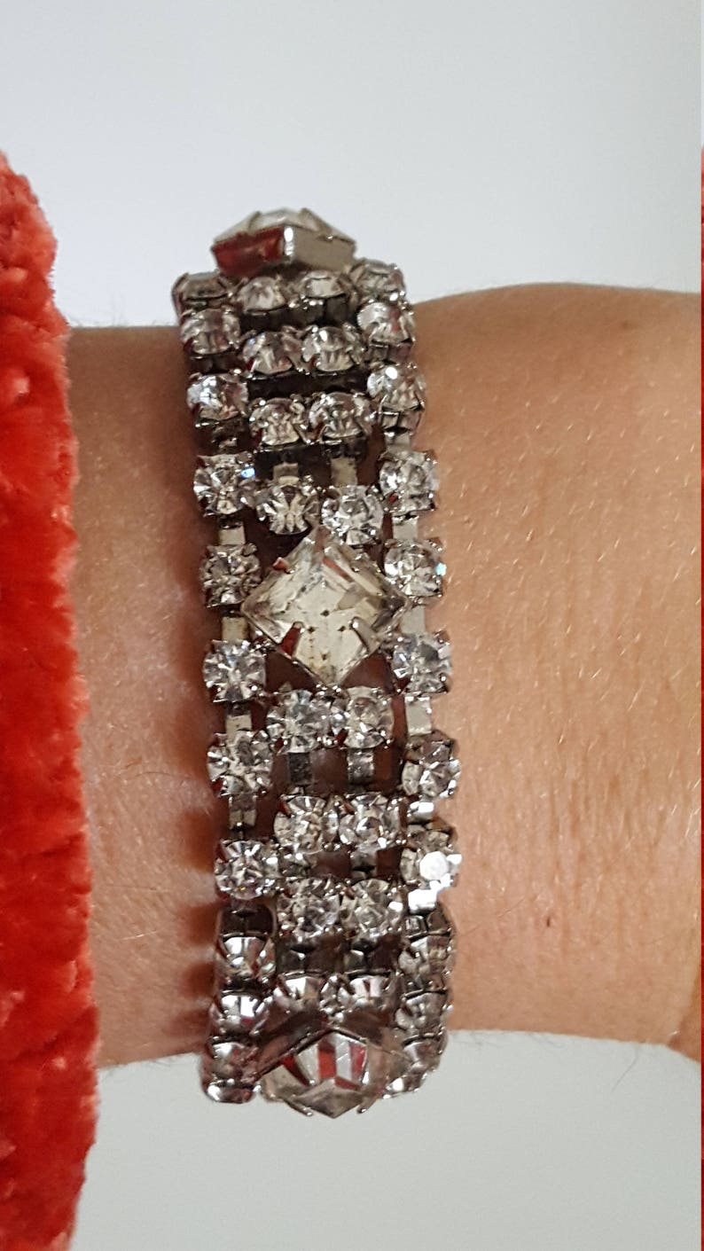 Peut inclure: Un bracelet argent&eacute; avec une rang&eacute;e de strass transparents. Le bracelet a un grand strass de forme carr&eacute;e au centre.