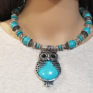 May include: A turquoise and silver owl pendant necklace. The necklace features a large owl pendant with turquoise stones and silver accents. The necklace is made of turquoise beads and silver spacers.