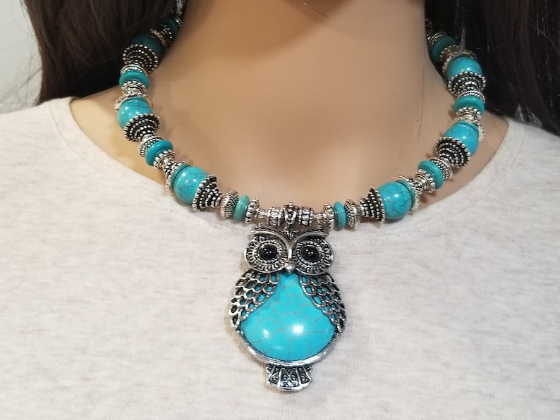 May include: A turquoise and silver owl pendant necklace. The necklace features a large owl pendant with turquoise stones and silver accents. The necklace is made of turquoise beads and silver spacers.