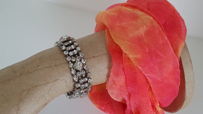 Peut inclure: Un bracelet argent&eacute; avec une rang&eacute;e de strass transparents. Le bracelet est sur un bras de mannequin avec une &eacute;charpe rose et orange.