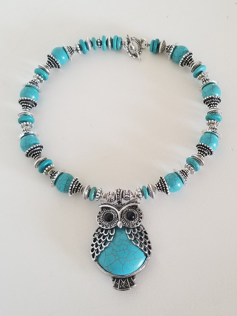 May include: A turquoise and silver necklace with an owl pendant. The owl has a turquoise body with silver detailing and black eyes.