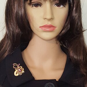 Puede incluir: Un broche dorado con un dise&ntilde;o floral y diamantes de imitaci&oacute;n morados. El broche se lleva en el cuello de una chaqueta negra.