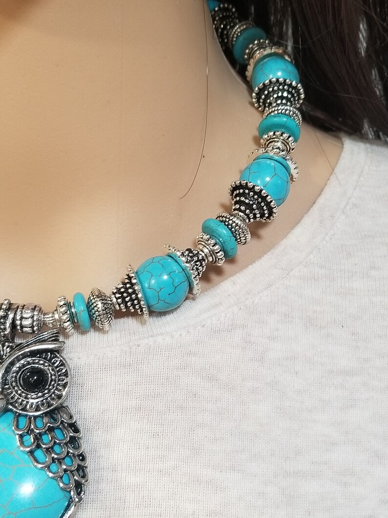 May include: A turquoise and silver owl pendant necklace. The necklace features a large owl pendant with turquoise stones and silver accents. The necklace is made of turquoise beads and silver spacers.