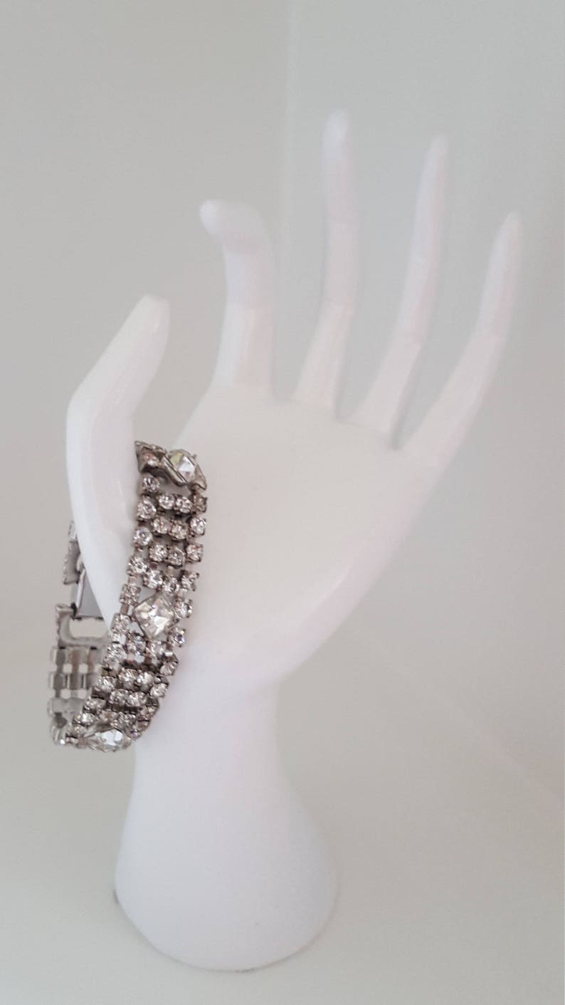 Peut inclure: Un bracelet argent&eacute; avec une rang&eacute;e de strass transparents. Le bracelet est sur une main de mannequin blanche.
