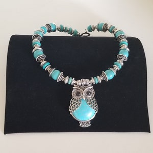 May include: A turquoise and silver necklace with an owl pendant. The owl has black eyes and is surrounded by turquoise stones.