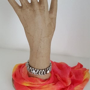 Peut inclure: Un mannequin de main en papier m&acirc;ch&eacute; portant un bracelet scintillant et une &eacute;charpe orange et rose vif.