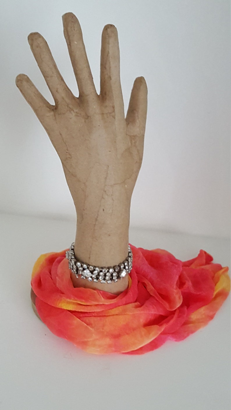Peut inclure: Un mannequin de main en papier m&acirc;ch&eacute; portant un bracelet scintillant et une &eacute;charpe orange et rose vif.