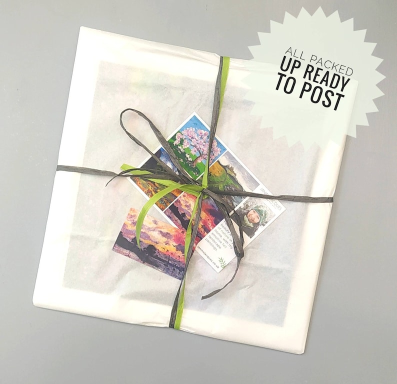 May include: Square package wrapped in white tissue paper, tied with dark gray and green ribbons. Small cards with landscape paintings are attached. The text "ALL PACKED UP READY TO POST" is on a starburst-shaped sticker.