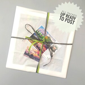 May include: A white package wrapped in tissue paper with a green and grey ribbon. The package has a business card attached with the text "Handcrafted with love in the heart of the Scottish Highlands" and a small card with a picture of a person. The package is labelled "All Packed Up Ready To Post".