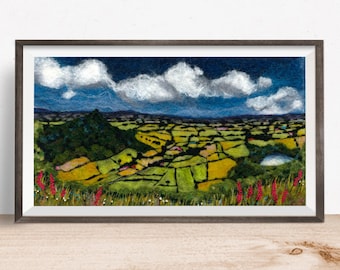 May include: A needle felted artwork depicting a rural landscape with rolling green hills, yellow fields, and a small lake. The sky is blue with fluffy white clouds. The artwork is framed in a dark gray frame.