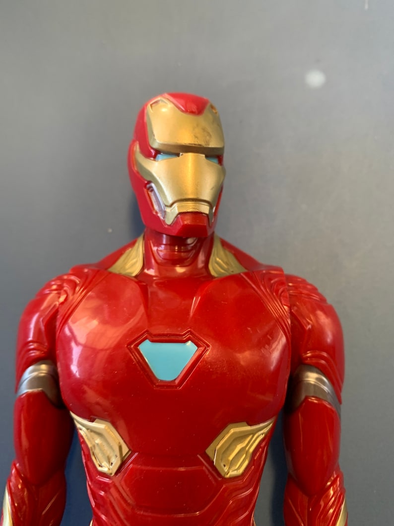 May include: A red and gold action figure of Iron Man, a superhero from the Marvel universe. The figure has a blue light in its eyes and a blue arc reactor on its chest.